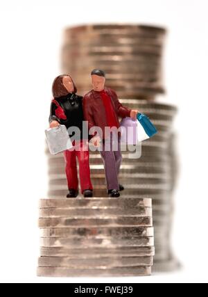 Un petit couple carrying shopping bags debout sur une pile de pièces. Banque D'Images