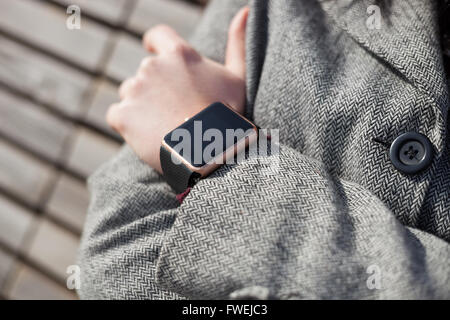 Femme en manteau gris portant des smart moderne montre-bracelet. Cette personne est toujours connecté à internet et médias sociaux même assis sur le banc. Banque D'Images