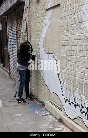 Une jeune femme artiste peindre une image abstraite sur un mur à Londres, Angleterre, Royaume-Uni. Banque D'Images