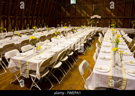 Des tableaux dans une vieille grange pour une réception de mariage, y compris le dîner. Ces rangées de tables sont prêtes à seta et servir plen Banque D'Images