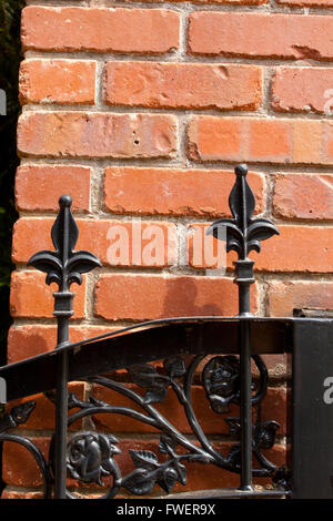Une barrière métallique en fer forgé avec un motif fleur de lis en haut est construit jusqu'à un mur de briques à un riche patrimoine. Banque D'Images