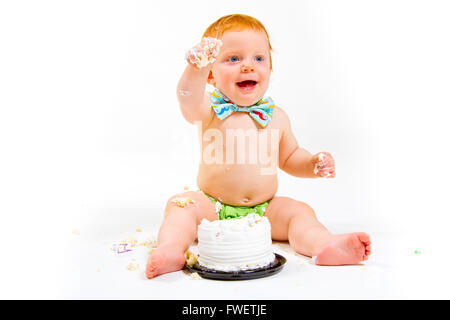 Un petit garçon arrive à manger gâteau pour la première fois sur son premier anniversaire à ce gâteau dans smash studio sur un fond blanc. Banque D'Images