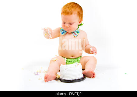 Un petit garçon arrive à manger gâteau pour la première fois sur son premier anniversaire à ce gâteau dans smash studio sur un fond blanc. Banque D'Images