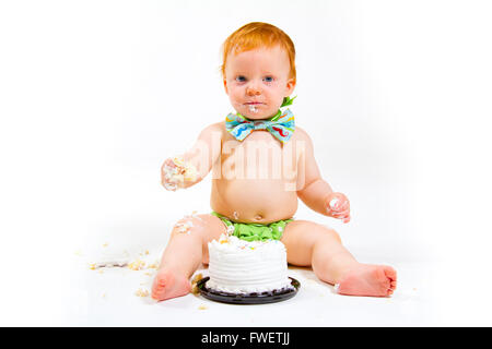 Un petit garçon arrive à manger gâteau pour la première fois sur son premier anniversaire à ce gâteau dans smash studio sur un fond blanc. Banque D'Images