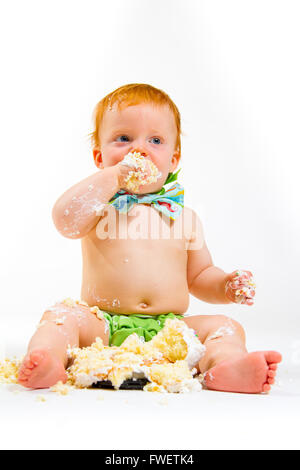 Un petit garçon arrive à manger gâteau pour la première fois sur son premier anniversaire à ce gâteau dans smash studio sur un fond blanc. Banque D'Images