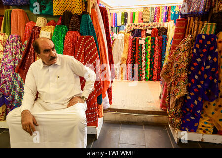 Assis à l'extérieur de son magasin commerçant entouré de matériaux colorés, Souq Waqif, Doha, Qatar, Moyen-Orient Banque D'Images