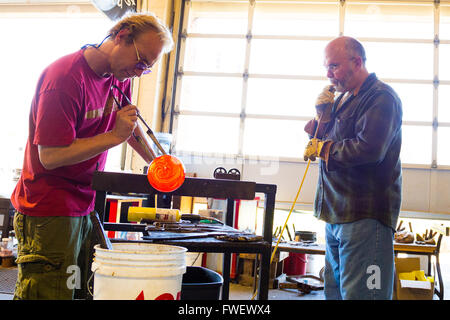 Deux hommes travaillent dur pour créer une pièce d'art unique de verre en fusion. Ils sont dans un studio de verre soufflé dans l'Oregon. Banque D'Images