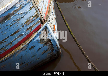 La coque d'un vieux bateau de pêche en bois construit à clins avec l'écaillage de la peinture rouge et bleu et corde d'amarrage. Banque D'Images