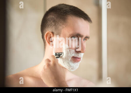 Portrait de beau jeune homme de son visage dans la salle de bain devant le miroir Banque D'Images