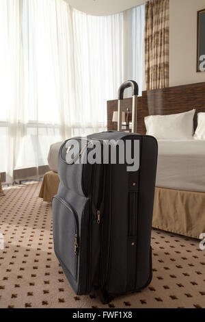 Grande valise à roulettes bleu debout sur le plancher dans la chambre d'hôtel. Vertical image Banque D'Images