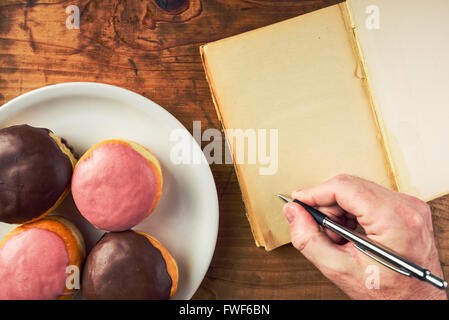 Recette pour écrire des délicieux beignets avec garniture sucrée, vue du dessus de la main des hommes dans l'ordinateur portable et de savoureux donuts Banque D'Images