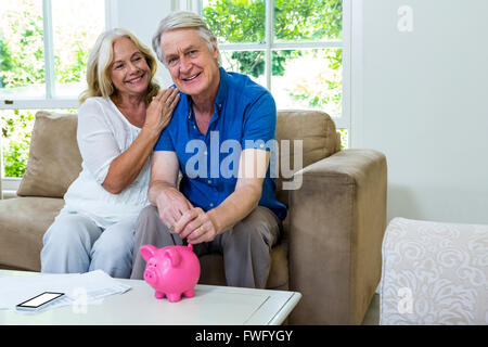 Happy senior couple putting coins in piggi à la maison de la banque Banque D'Images