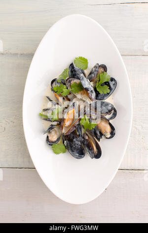 Moules dans une assiette blanche sur fond de bois Banque D'Images