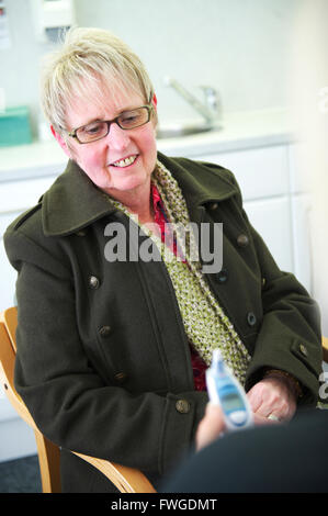 La femme d'âge moyen à la discussion des résultats heureux avec Médecin Généraliste (GP) dans la chirurgie du NHS Banque D'Images