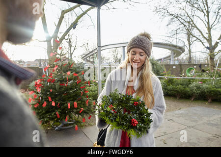 Une femme tenant une couronne de la décoration de Noël dans un centre de jardinage. Les arbres de Noël dans l'arrière-plan. Banque D'Images