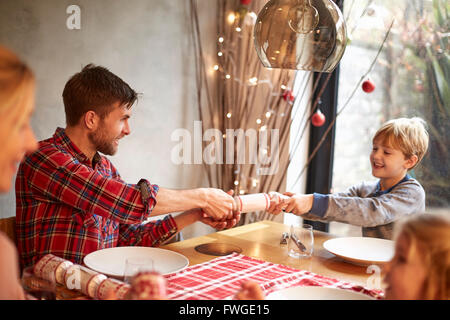 Une famille de quatre personnes, deux adultes et deux enfants assis autour d'une table à l'époque de Noël, tirant sur des craquelins. Banque D'Images