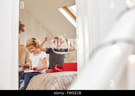 Le matin de Noël dans une maison familiale. Une mère et deux enfants assis sur un lit de l'ouverture des cadeaux. Banque D'Images