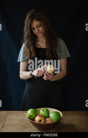 Une femme en tablier bleu peeling une pomme avec un couteau. Banque D'Images