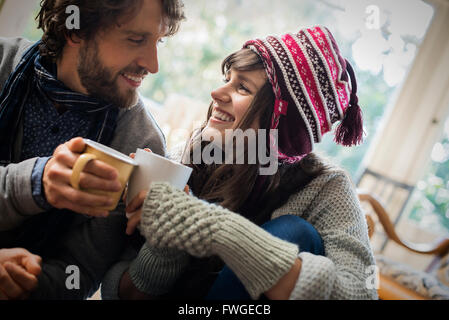 Un couple, homme et femme assis près l'un de l'autre l'échauffement avec leurs mains autour de tasses. Banque D'Images