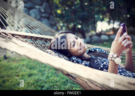 Une femme couchée dans un hamac de jardin en tenant vos autoportraits avec son téléphone. Banque D'Images