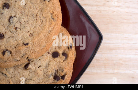 Haut de page Fermer la vue de deux chocolate chip cookies sans gluten sur une plaque rouge profond au sommet d'une table en bois. Banque D'Images