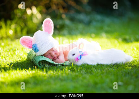 Mignon bébé nouveau-né garçon en costume de lapin wearing hat avec les oreilles et blanc couche et un vrai lapin à sunny jardin vert Banque D'Images