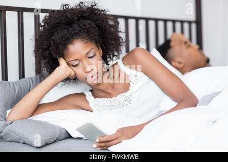 Young woman using mobile phone while man sleeping on bed Banque D'Images