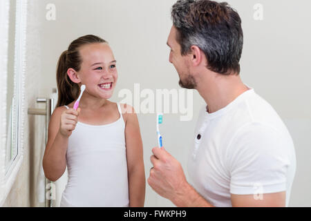Père et fille souriante tenant une brosse à dents dans la salle de bains Banque D'Images