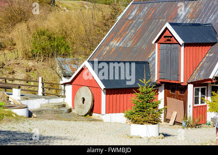 Kivik, Suède - 1 Avril 2016 : Un millwheel est appuyé contre une ferme en bois rouge. Cour de gravier avec une épinette en face de Banque D'Images