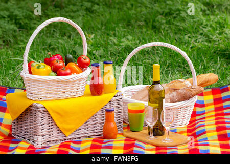Pique-nique sur l'herbe. Panier pique-nique avec des légumes et du pain. Une bouteille de vin avec des verres et des bouteilles de jus. Banque D'Images
