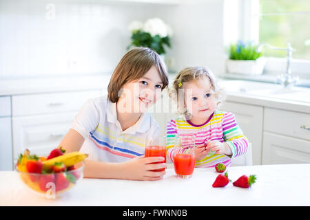 Heureux adolescent garçon et de sa soeur enfant mignon de fruits pour le petit déjeuner avant d'avoir l'école et boire du jus de maternelle Banque D'Images