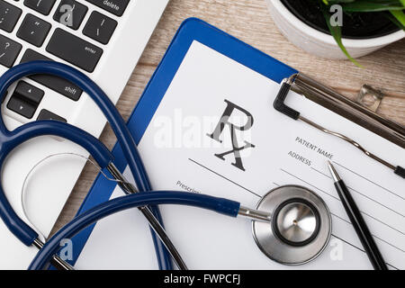 Close-up Vue de dessus du chimiste pharmaceutique place de travail. Stéthoscope, ordinateur portable et forme d'ordonnance en blanc sur la surface en bois. Il Banque D'Images