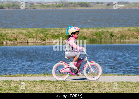 Une jeune fille hispanique avec une licorne helmit rides son vélo sur les sentiers du lac Overholser, Oklahoma City, Oklahoma, USA. Banque D'Images