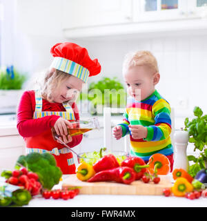 Enfants dans la cuisine une salade de légumes frais dans une cuisine blanche. Faire cuire les légumes pour les enfants déjeuner végétarien. Banque D'Images