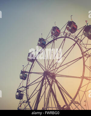 Une grande roue tourne à un carnaval au coucher du soleil pour une activité artistique ou concept de mémoire d'été. Banque D'Images