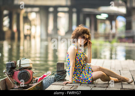 Femme asiatique à la mode assis sur un quai de la rivière en bois. Banque D'Images