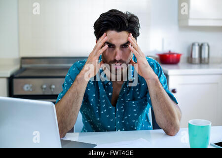 Tendu homme assis avec des factures et l'ordinateur portable dans la cuisine Banque D'Images