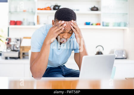 Tendue young man sitting in kitchen with laptop Banque D'Images