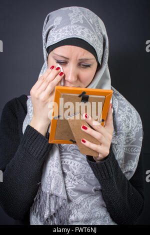 Femme musulmane gémissant sur une vieille photographie dans un cadre Banque D'Images