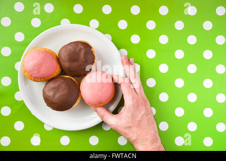 Cueillette à la main des hommes avec une garniture aux fraises beignets sucrés à partir d'une plaque, vue de dessus des délicieux donuts sur table de cuisine à pois Banque D'Images