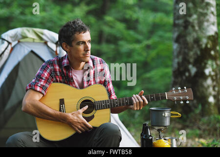 Caucasian man à jouer de la guitare à un camp site Banque D'Images