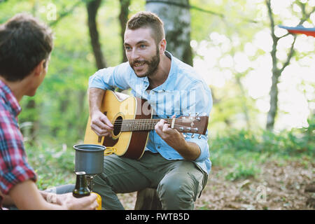 Les amis à jouer de la guitare à un camp site Banque D'Images