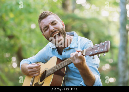 Caucasian man à jouer de la guitare à un camp site Banque D'Images