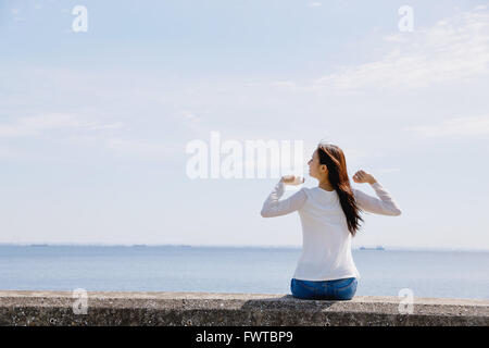 Jeune japonaise assis sur mur en béton par la mer Banque D'Images