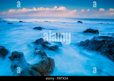 Vagues sur les rochers de la plage au lever du soleil à Napili Bay avec en arrière-plan, Maui Molokai Banque D'Images