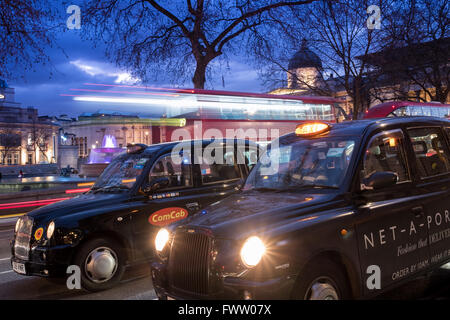 Deux taxis et un autobus à Londres, Trafalgar Square au crépuscule. Banque D'Images
