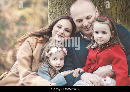 Les parents avec leurs deux petites filles se détendre sous tree in park Banque D'Images