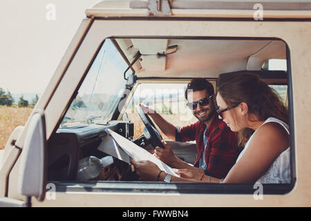 L'homme et la femme sur un voyage sur la route et la lecture d'un site, tandis qu'assis à l'intérieur de leur voiture. Happy young couple on road trip.
