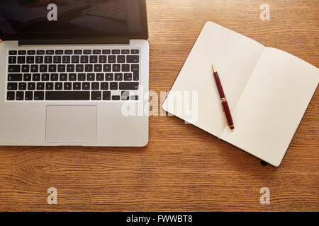 Vue de dessus d'un ordinateur portable avec le journal intime et stylo et sur table en bois. Vue de dessus de bureau. Banque D'Images