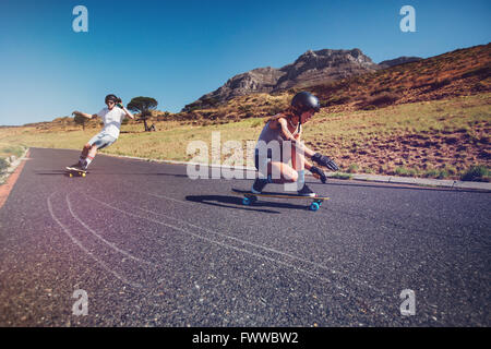 Deux jeunes gens pratiquant en plein air équitation conseil long on rural road. L'homme et la femme longboard sur une journée d'été. Banque D'Images